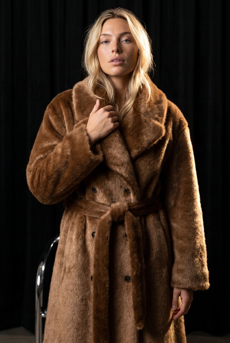 Brown belted faux fur coat clutched at the collar in the Noir Chrome studio