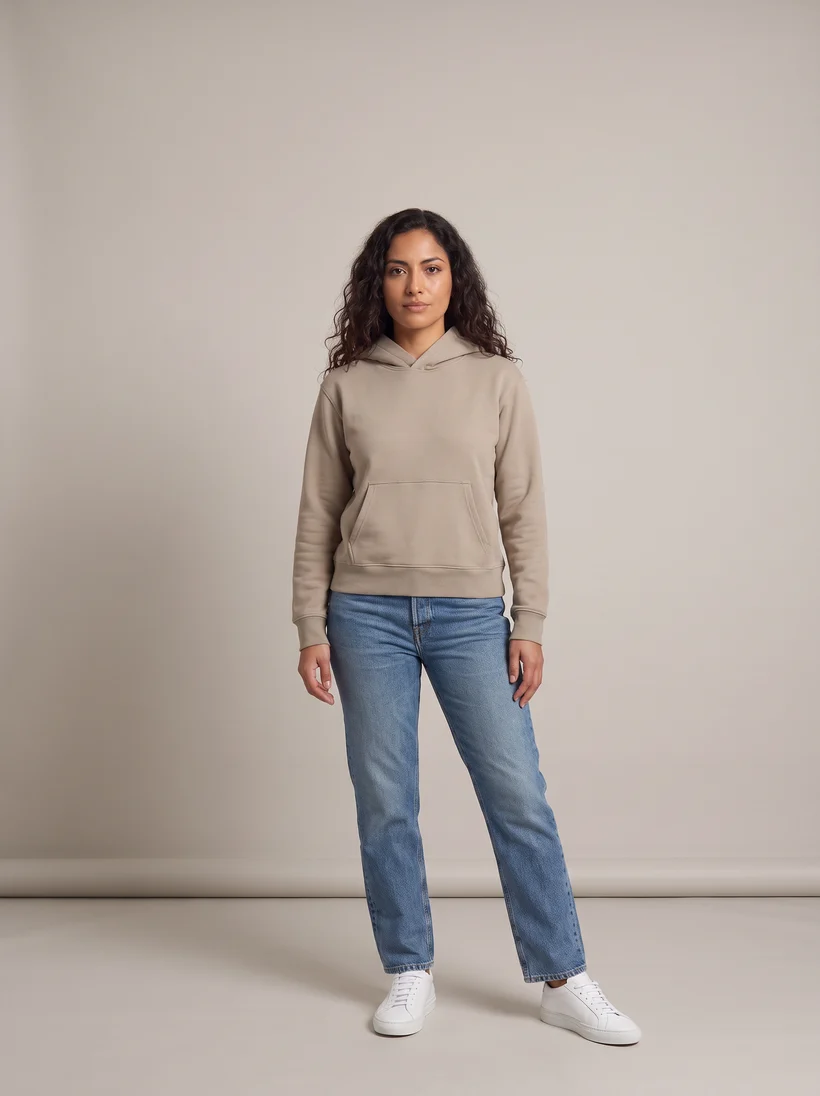 Model standing and facing the camera in a taupe hoodie, straight jeans and white sneakers on a warm grey paper backdrop, the front pose of the original shoot, generated with Gemini Pro