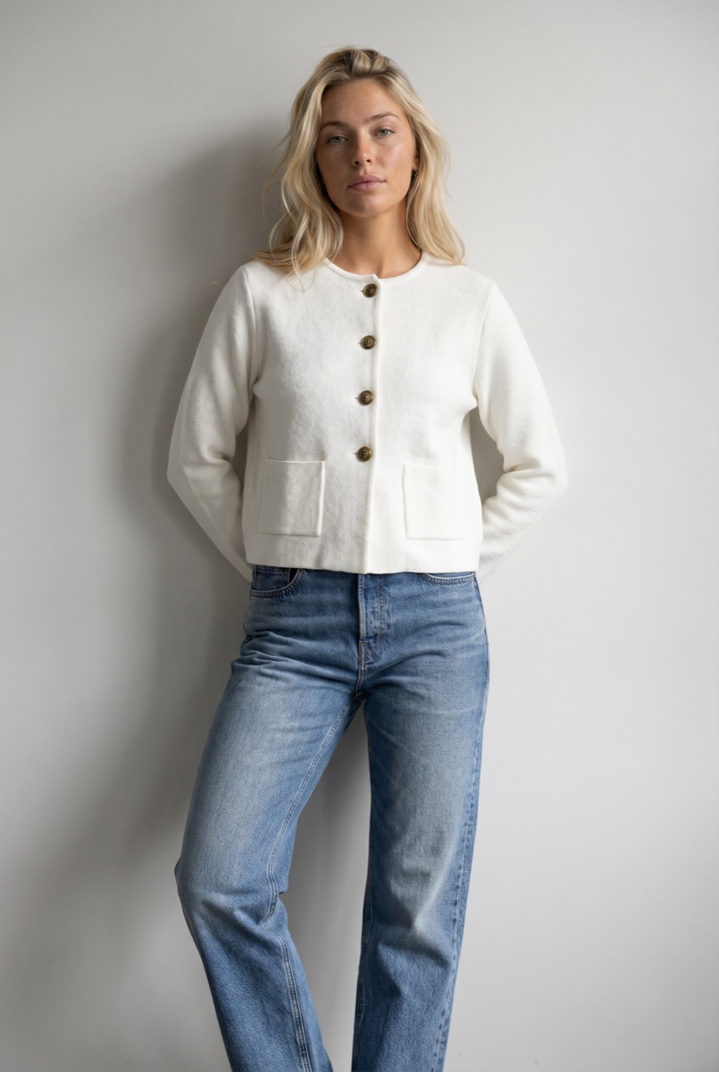 Model wearing a cropped white jacket with relaxed denim jeans, approved by QA