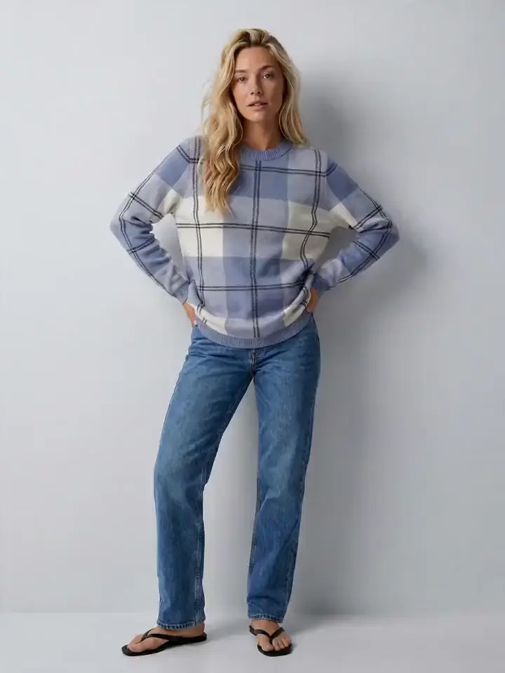First frame of a Seedance clip of the same saved AI model in the same check sweater and jeans on the same set