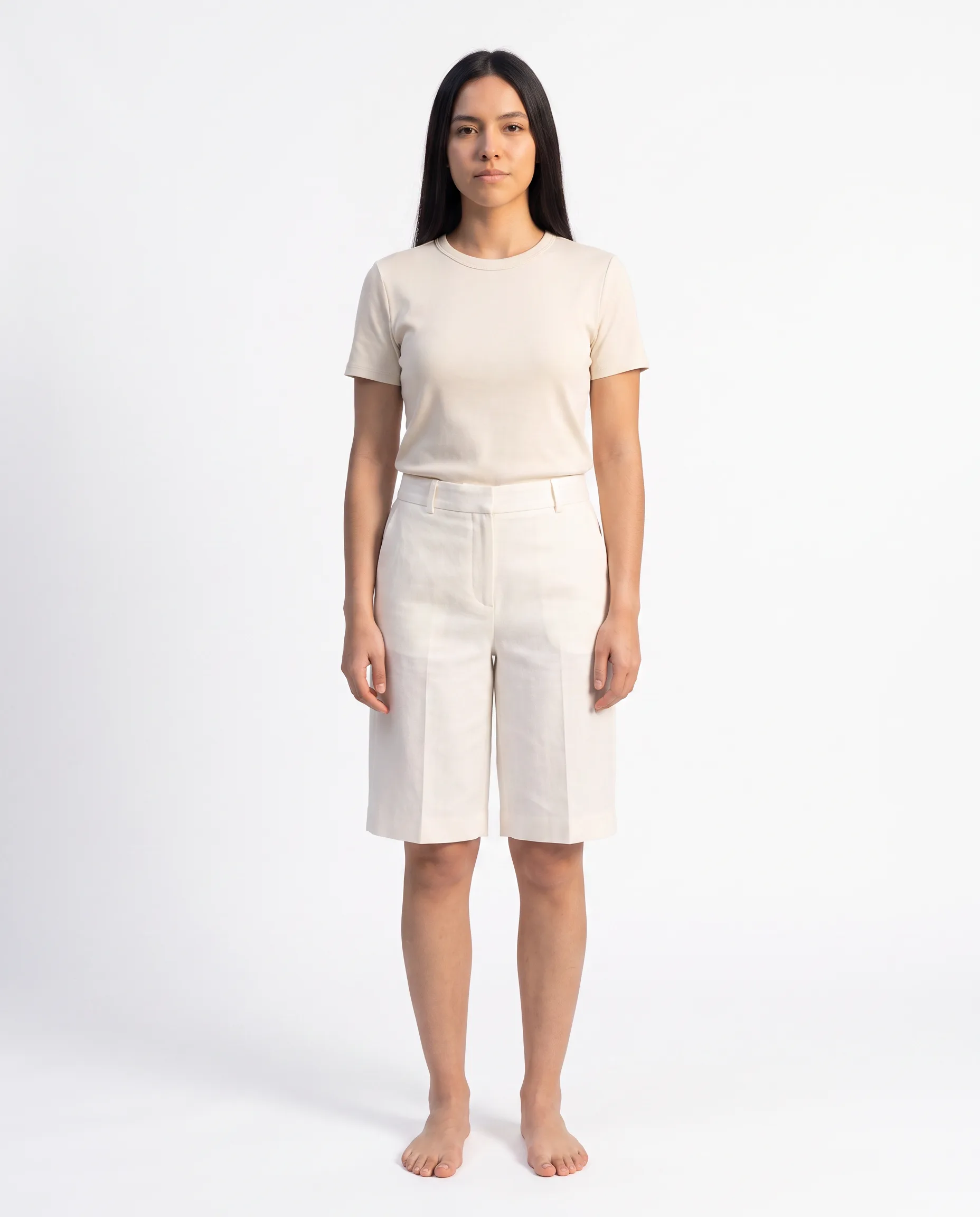 Front view of a female model wearing cream tailored knee-length shorts against a studio backdrop
